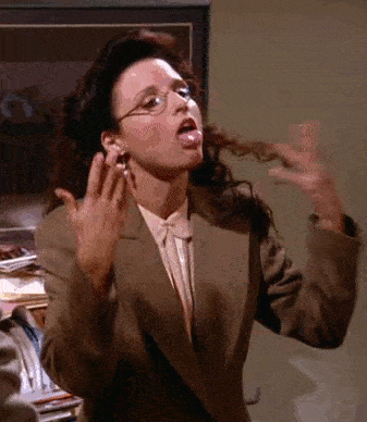 A woman with dark hair and glasses, wearing a brown blazer and pink blouse, dramatically fans herself with both hands, appearing to be flustered or overwhelmed. She is standing in a cluttered office space. - Choice Hacking Academy A woman with dark hair and glasses, wearing a brown blazer and pink blouse, dramatically fans herself with both hands, appearing to be flustered or overwhelmed. She is standing in a cluttered office space.